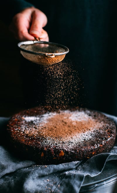 hand sifting cocoa over a flat cake