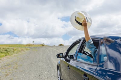 person waving hat out window of car