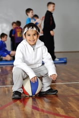 Young boy sitting on basketball, his friends in background